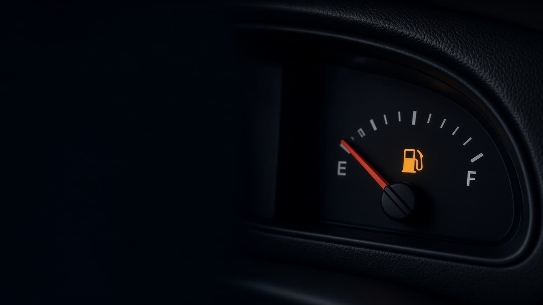 Car fuel gauge at night with the needle on empty and the low-fuel light on